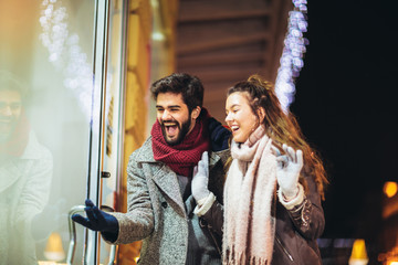 Couple with gift bag on Christmas lights background during walking in the city at evening. Window shopping.