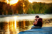 Father And 2 Years Old Child Play Fishing On Bank Of Lake In Sunset Time. Golden In Sun Light Trees And Water Around. Father And Daughter Son Fun Together. Lesson Of Fishing In Evening Time. Weekend