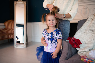 Mother brushing a hair of her little daughter in a beutiful dress at home