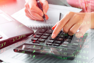 Closeup of the hand of a girl who uses a calculator to calculate data and to analyze the stock market. Freelance, work from home, online trading concept