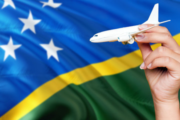 Wall Mural - Solomon Islands travel concept. Woman holding a miniature plane on national flag background. Holiday and voyage theme with copy space for text.