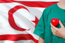 Northern Cyprus Veterinary Clinic Concept. Veterinarian Is Holding Plastic Heart In Green Uniform On National Flag Background. Animial Love Theme.