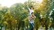 © Rapeepat - Asian family Father and son sat on his shoulders and run in the park. With paper plane as a toy in the hands of children And there are many big trees in the garden Is natural in the morning of summer