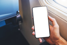 Mockup Image Of A Hand Holding A Black Mobile Phone With Blank Desktop Screen Next To An Airplane Window