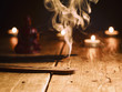Smoking incense stick in the foreground. On background Small statue of Buddha with incense sticks and burning candles