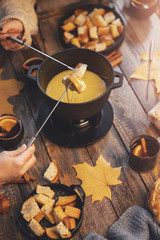 Girl cooks gourmet Swiss fondue dinner with cheese on fire, autumn wooden background with maple leaves. Top view, flat lay