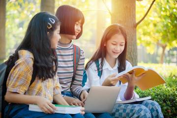 Wall Mural - Three asian teenager student sitting in park and using notebook computer for doing homework together