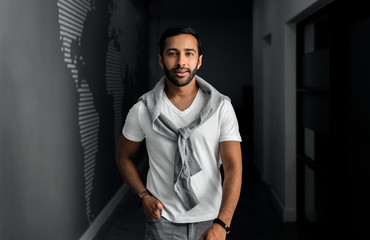 Handsome Gen z Indian arabic man walking through walkway wearing white t-shirt and grey cardigan over his shoulders