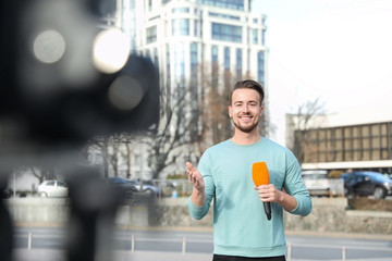 Wall Mural - Young male journalist with microphone working on city street