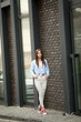 © ElenaBatkova - Stylish young woman in white jeans walks and bounces on city streets against brick wall.