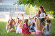 © Andrey - children hold a lesson with the teacher in the park on a green lawn.