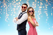 valentines day, love and people concept - happy couple in heart-shaped sunglasses over holiday lights on blue background