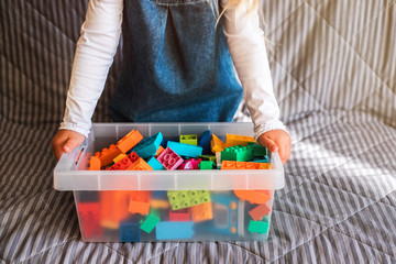 Little girl cleaning up the toy box at home. Child's space organization.