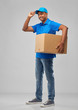 mail service and shipment concept - happy indian delivery man with parcel box in blue uniform over grey background