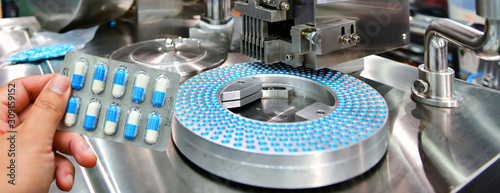 Photographie Hand holding blue capsule pack at medicine pill production line, Industrial pharmaceutical concept