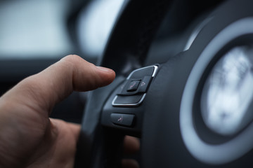 Close-up of male hand presses button of phone on steering wheel of car.