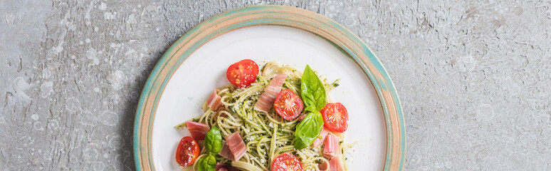 Wall Mural - top view of cooked Pappardelle with tomatoes, basil and prosciutto on plate on grey surface, panoramic shot