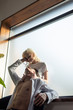 © LIGHTFIELD STUDIOS - Smiling woman embracing shirtless boyfriend while sitting on windowsill