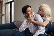 © LIGHTFIELD STUDIOS - Smiling young couple hugging and holding hands on sofa in living room