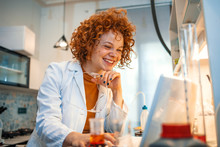 Confident Female Scientist Working On Laptop In Chemical Laboratory. Young Medical Student Learning And Writes In Laboratory. Woman Working A Scientist And Making Experiments