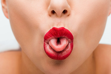 Wall Mural - cropped view of young woman with red lips sticking out tongue isolated on white