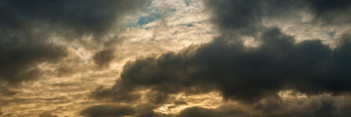 Wall Mural - wide panoramic view of the cloudy sky with gray clouds, orange scarlet from below and skylight from above