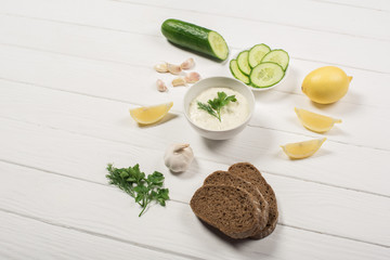 Canvas Print - Delicious tzatziki sauce with fresh ingredients and bread on white wooden background