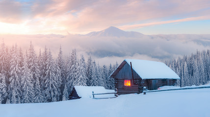 Wall Mural - fantastic winter landscape with wooden house in snowy mountains. hight mountain peaks in foggy sunse