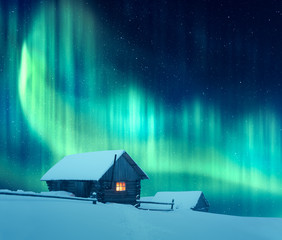 Wall Mural - fantastic winter landscape with wooden house with light in window in snowy mountains and northen lig