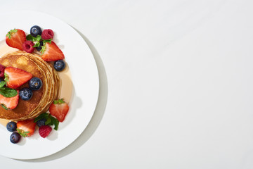 Wall Mural - top view of delicious pancakes with maple syrup, blueberries and strawberries on plate on marble white surface