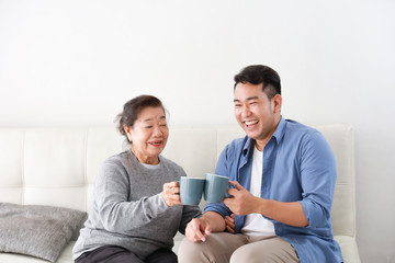 Wall Mural - Asian senior grand mother and son drinking coffee and talking happy and smile face in living room