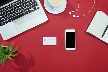 Poster - top view of credit card, smartphone, laptop, earphones, coffee, notebook and plant on red background
