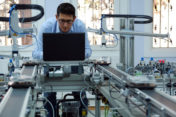 Focus on Gripper which picks up the product from an automated car and programming engineer at the background. Industry 4.0 workshop in an automation education center. Engineer is programming PLC.