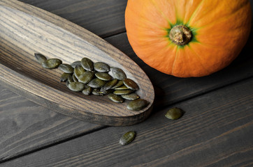 Raw organic green pumpkin seeds in wooden plate with pumpkin on wooden dark background