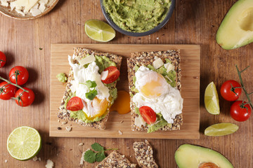 Wall Mural - bread slice with avocado, poached egg, tomato and cheese on wooden board