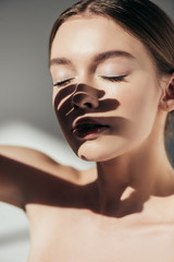 Wall Mural - portrait of nude girl with closed eyes and shadows on face on grey