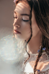Wall Mural - tender girl with braids in hairstyle posing in white boho dress on grey with lens flares