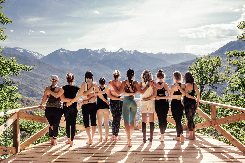 Rear view of a group of slim body-positive sportive active friendly women doing fitness and yoga together among mountain ecologically clean nature. Ecological Sports Tourism Concept - obrazy, fototapety, plakaty 