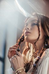 Wall Mural - attractive thoughtful girl with braids in hairstyle posing in white boho dress on grey with lens flares