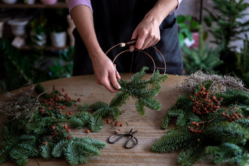 Woman making Christmas wreath of spruce, step by step. Concept of florist's work before the Christmas holidays..