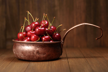 rustic copper ladle with sweet cherry on a wooden background