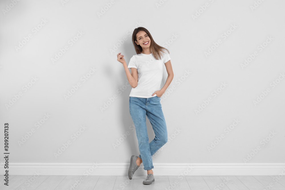 Young woman in stylish jeans near light wall - obrazy, fototapety, plakaty 