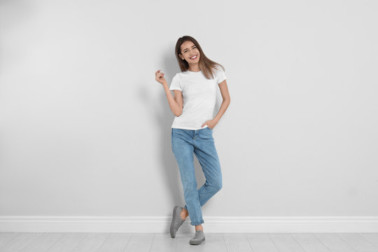 young woman in stylish jeans near light wall