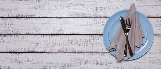 Wall Mural - Blue plates, napkin and cutlery on an old white wooden background.