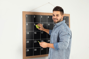 Wall Mural - Young man putting sticky note on board calendar