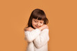 © Marharyta Hanhalo - Self love, little child pretty girl hugging herself. Comfort zone, pleasure, cozy concept. Cheerful charming caucasian child in white sweater over orange background.