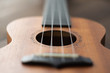 Defocused ukulele strings body, soundhole, bridge and neck on brown wooden background.