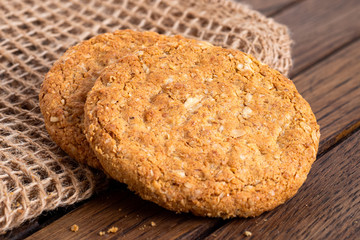 Two crunchy oat and wholemeal biscuits lying on brown burlap on dark wood.