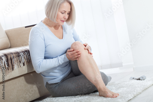 Fotomural Middle-aged woman suffering from pain in leg at home, closeup