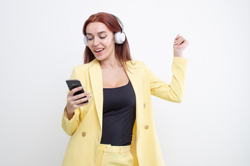 Wall Mural - A red haired girl in a yellow suit listens to music in large headphones and types on the phone